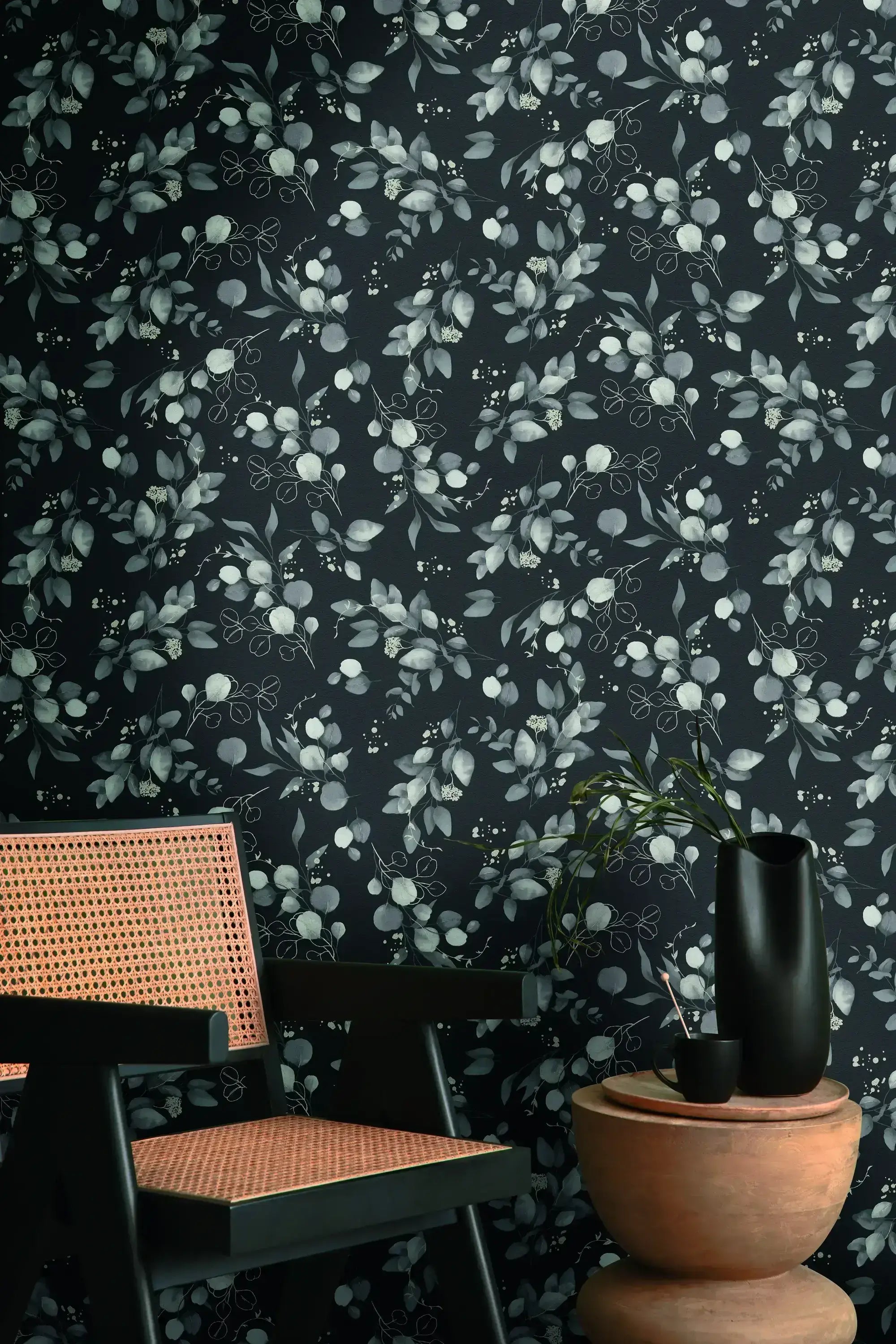Et rum med vægdekoration af Botanic Elegance - Noir tapet, der viser et botanisk mønster, ved siden af en stol og en vase.