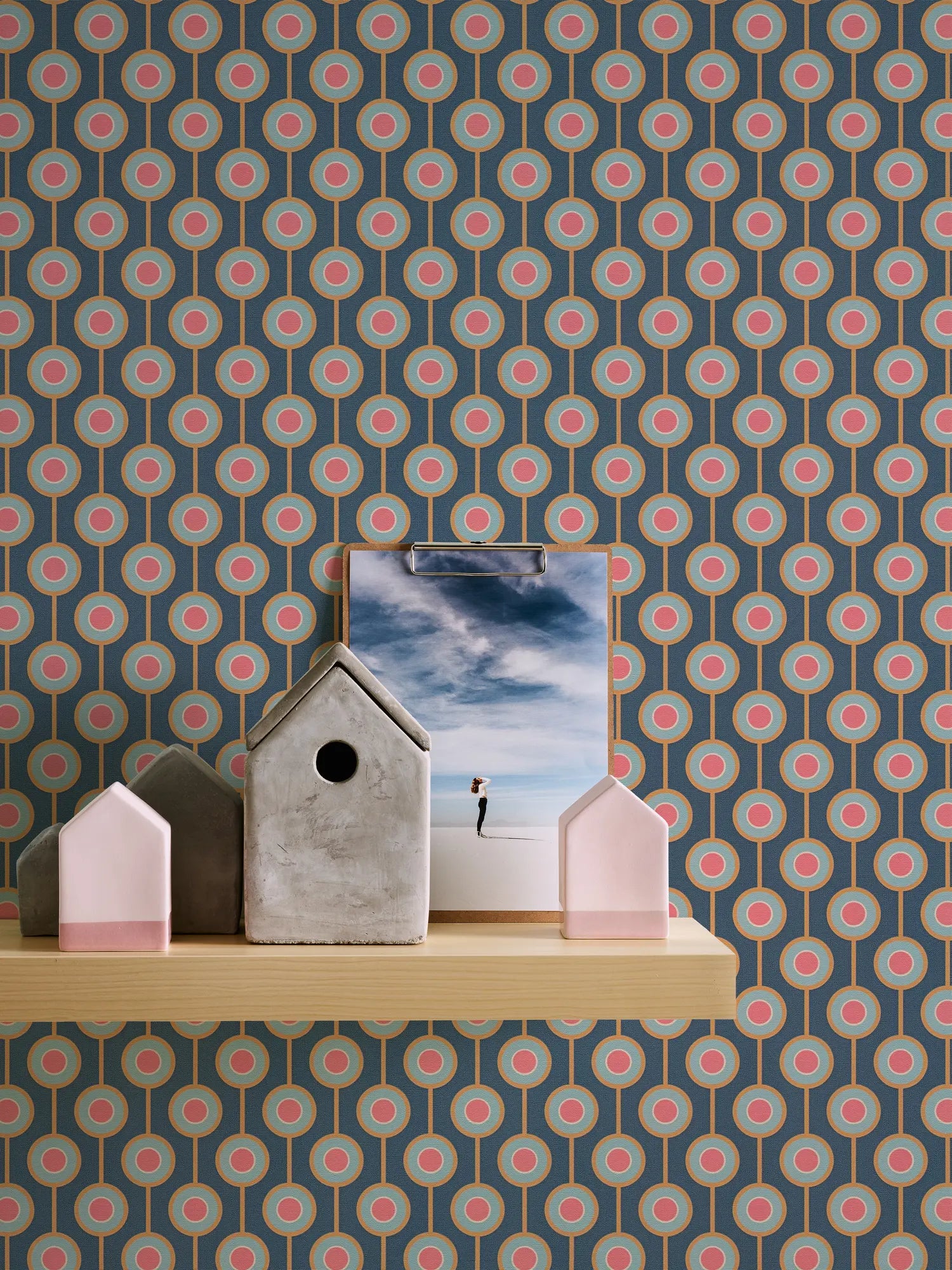 Cynthia - Vintage Teal tapet som baggrund for en hylde dekoreret med små husfigurer og et billede.