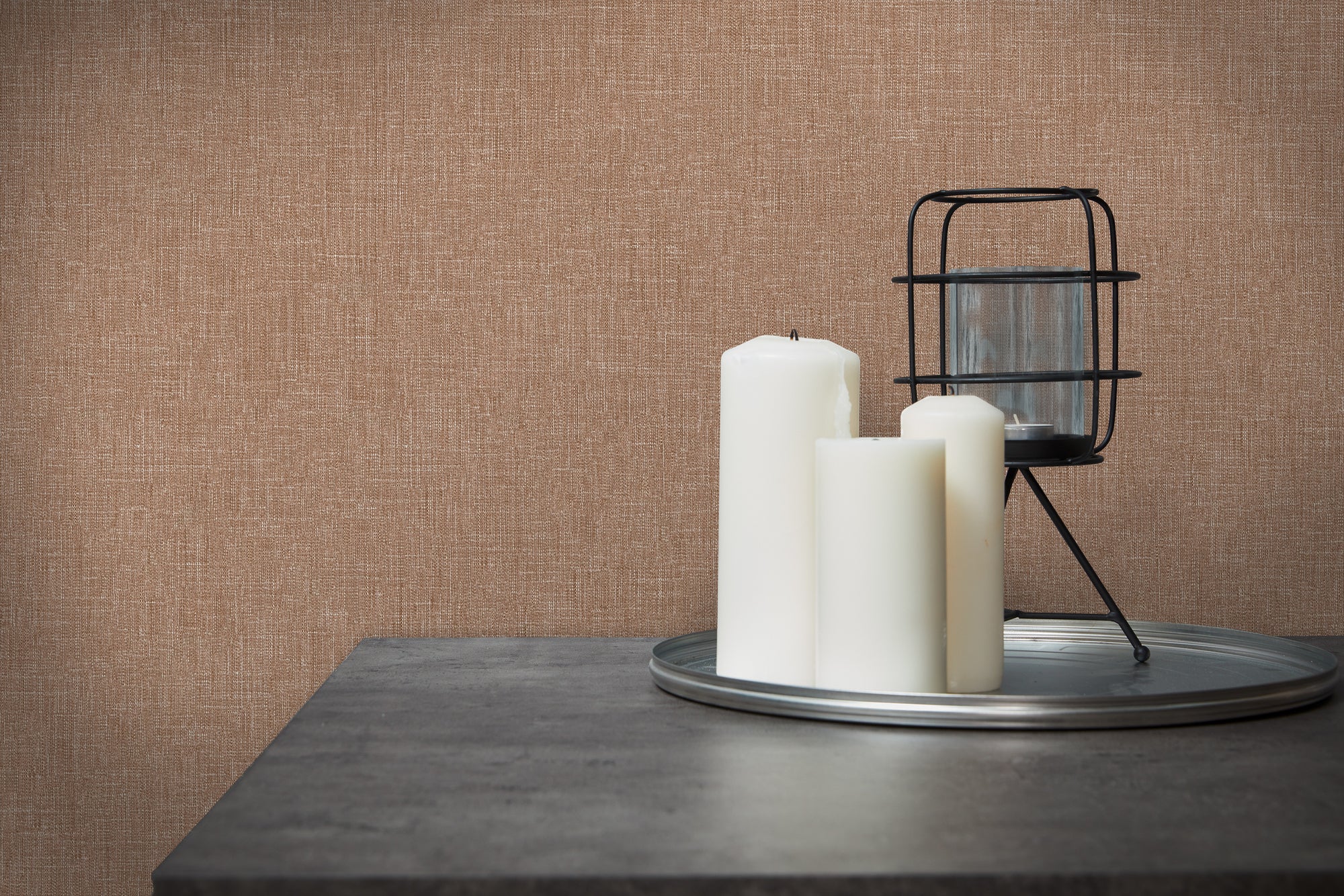 Indretning med Emily's Effect - Dune tapet som baggrund, der viser tekstur og varme, brune nuancer bag hvide stearinlys på et bord.