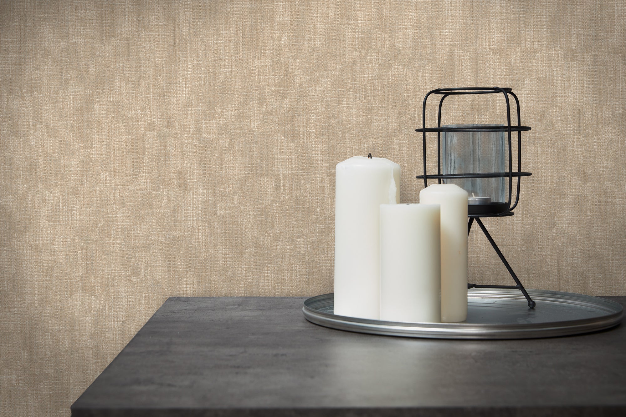 Emily's Effect - Sand tapet i et interiør med et stilleben af hvide stearinlys og en sort lysestage på en grå bordoverflade.