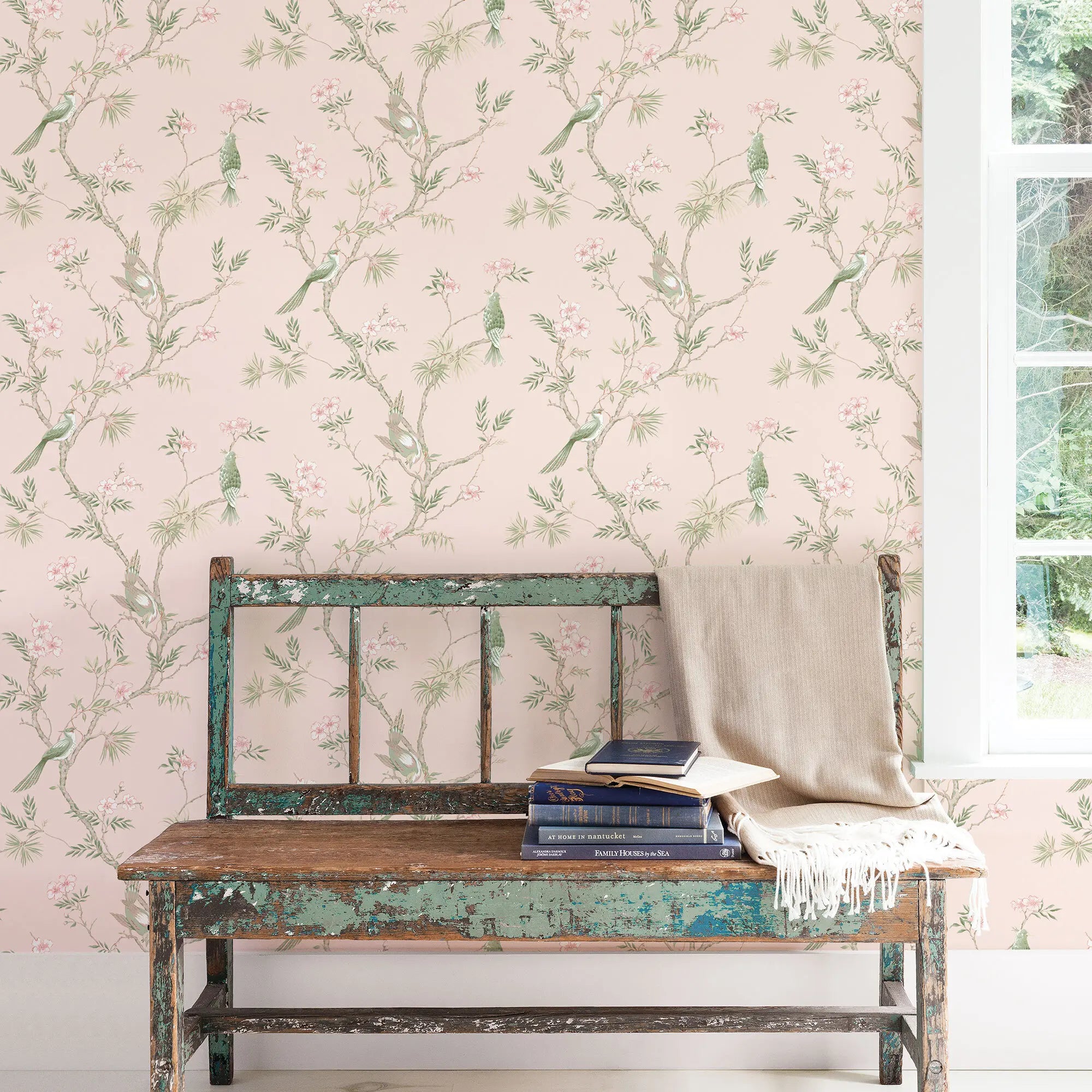 Billedet viser Veiled Aviary - Blossom tapet som baggrund i et rum med en rustik bænk og bøger ved siden af et vindue.