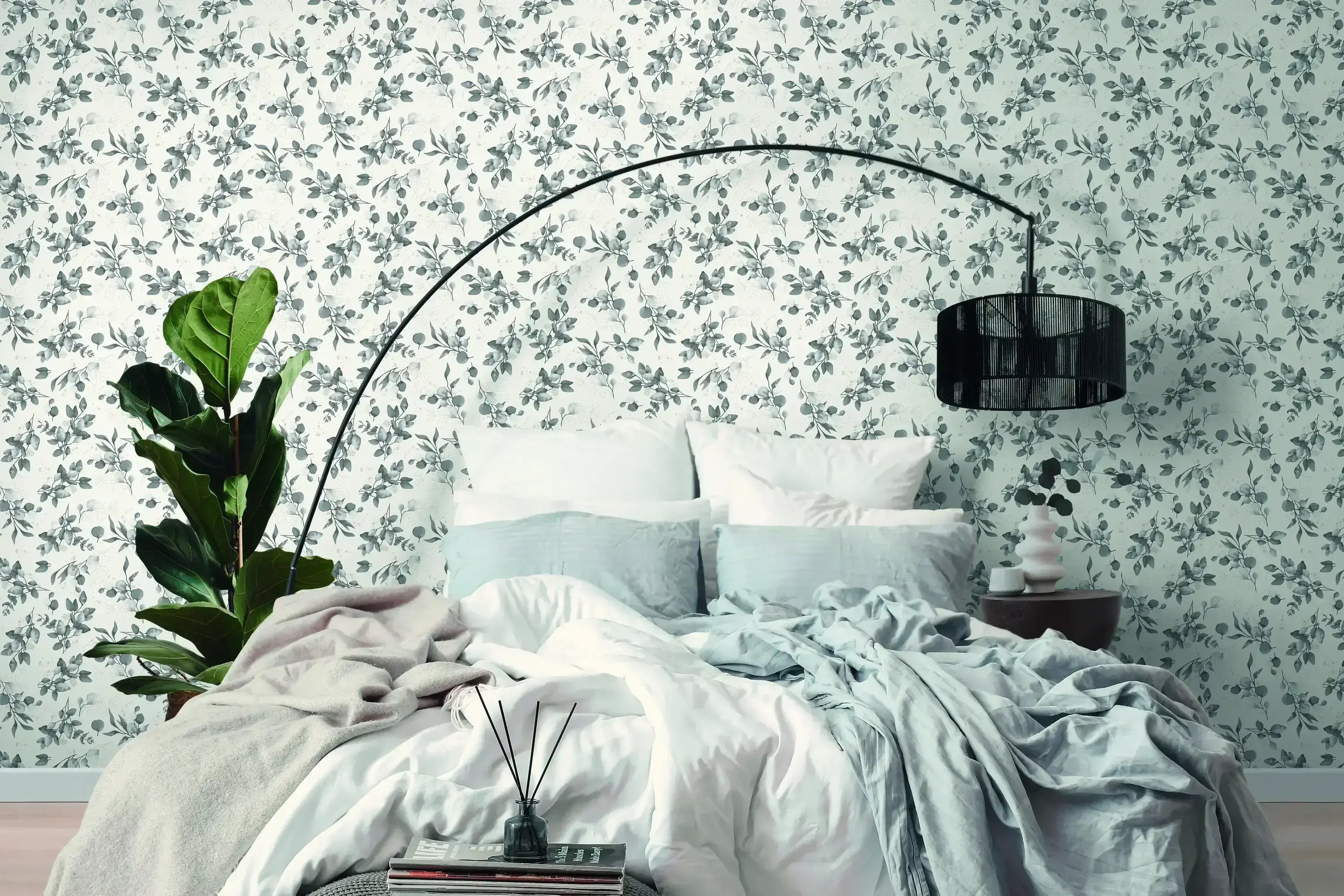 Soveværelse indrettet med tapet Botanic Elegance - Silver, der har et blomstret mønster i sølvagtige toner, bag en seng med hvide og blå sengetæpper.