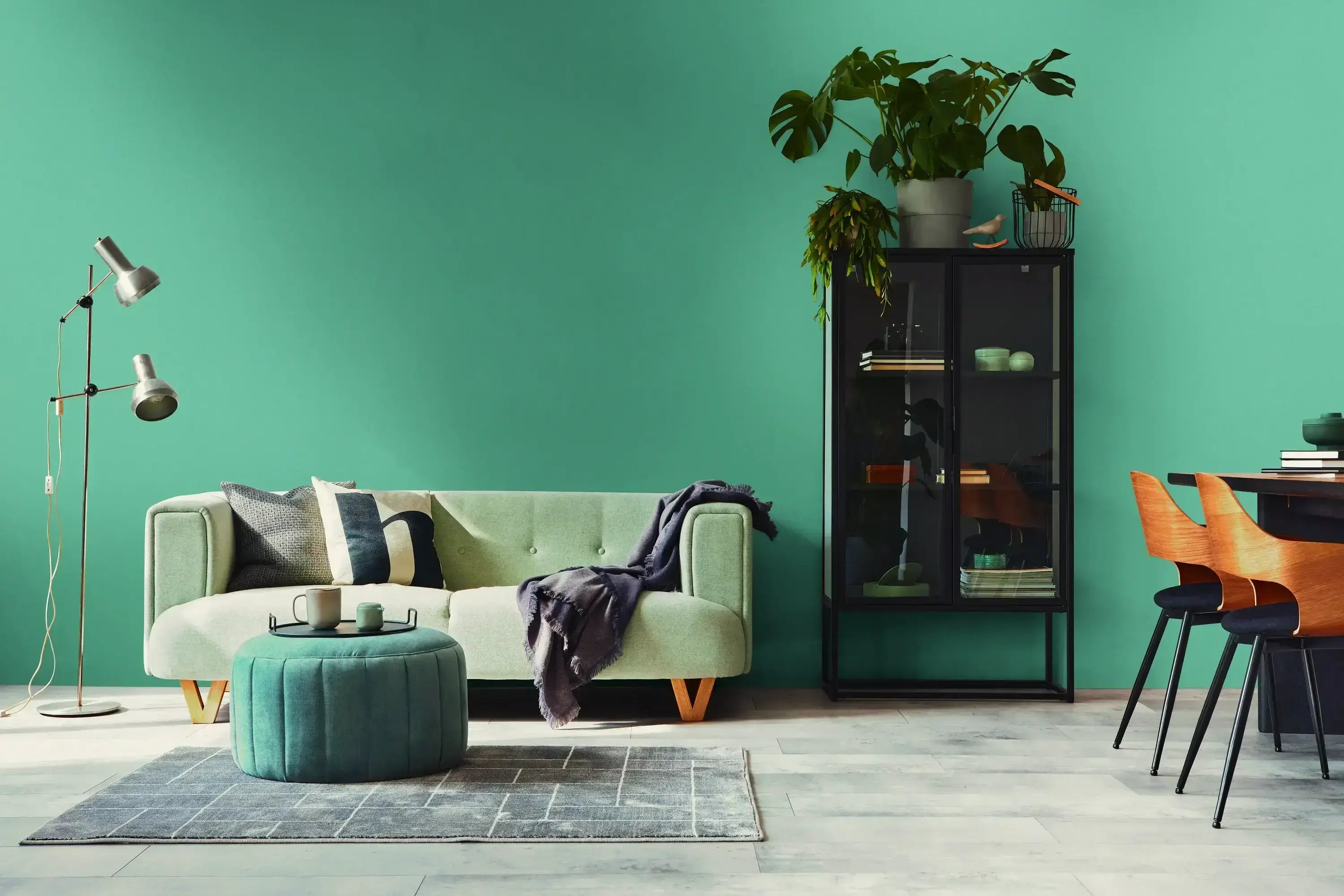 En moderne stue med Serene Elegance - Azure tapet. Der er en lysegrøn sofa, et rundt puf i samme tone, og en sort opbevaringsenhed. Grønne planter tilføjer liv til rummet.