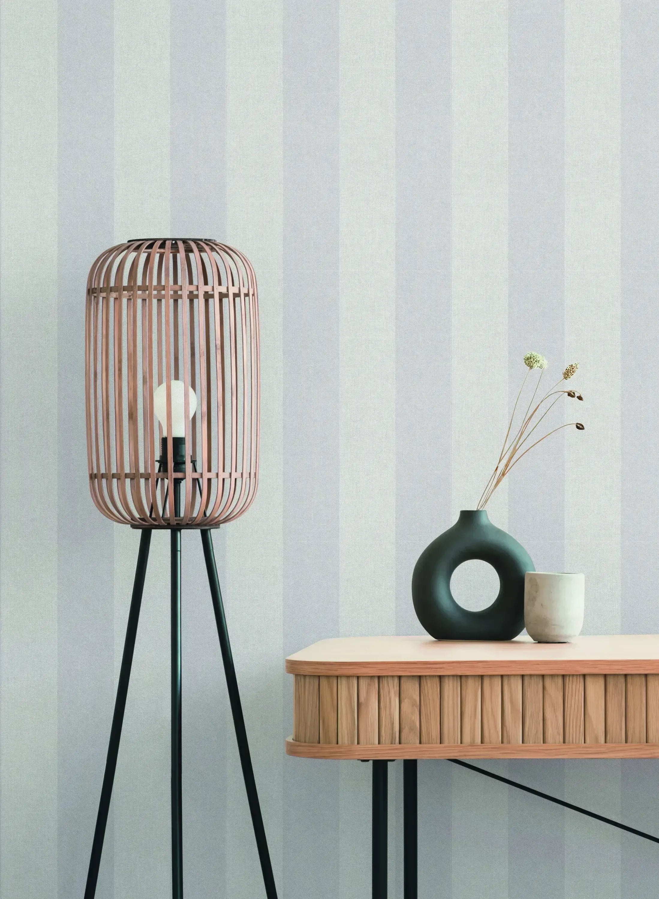 Interiørbillede med Striped Elegance - Dusk tapet fra Nicetapet.dk, der viser en moderne lampe og bord mod en væg med lyse striber.